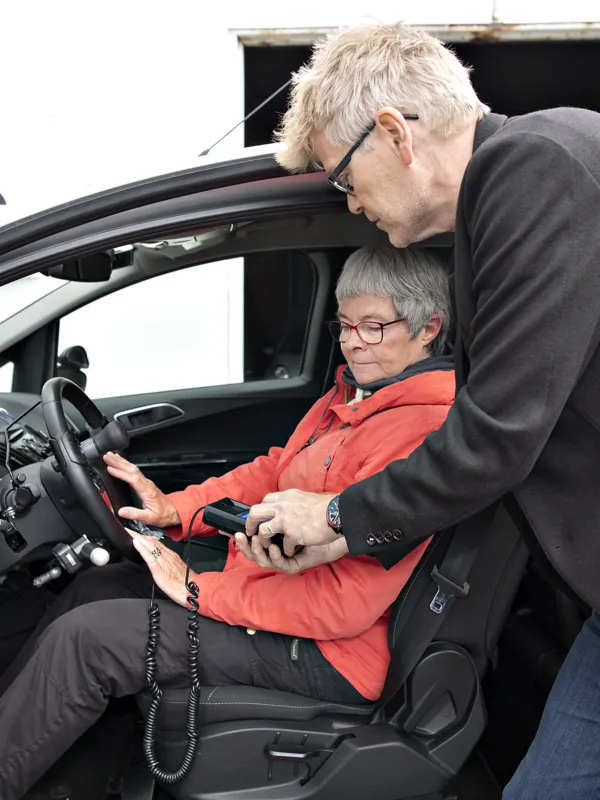 En kvinde sidder i en af HandicapBilistCentrets koerevogne, mens en ansat i HandicapBilistCentret tester indretningen.